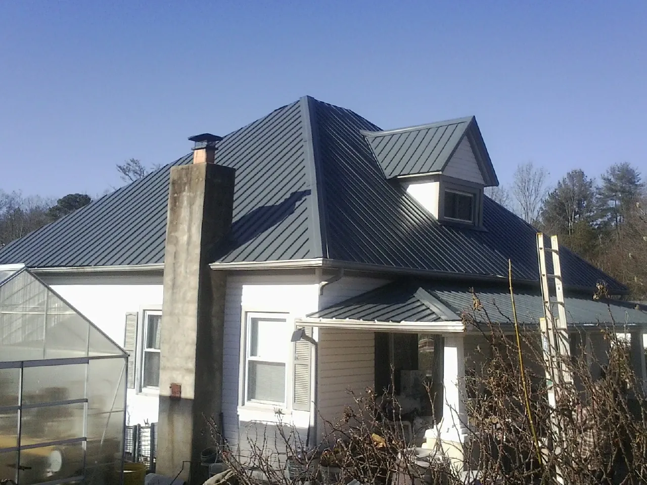 Dark blue standing seam metal roof on a white farmhouse with dormer — Slate & Tile Roof Repair by Roofing Brothers in Old Westbury
