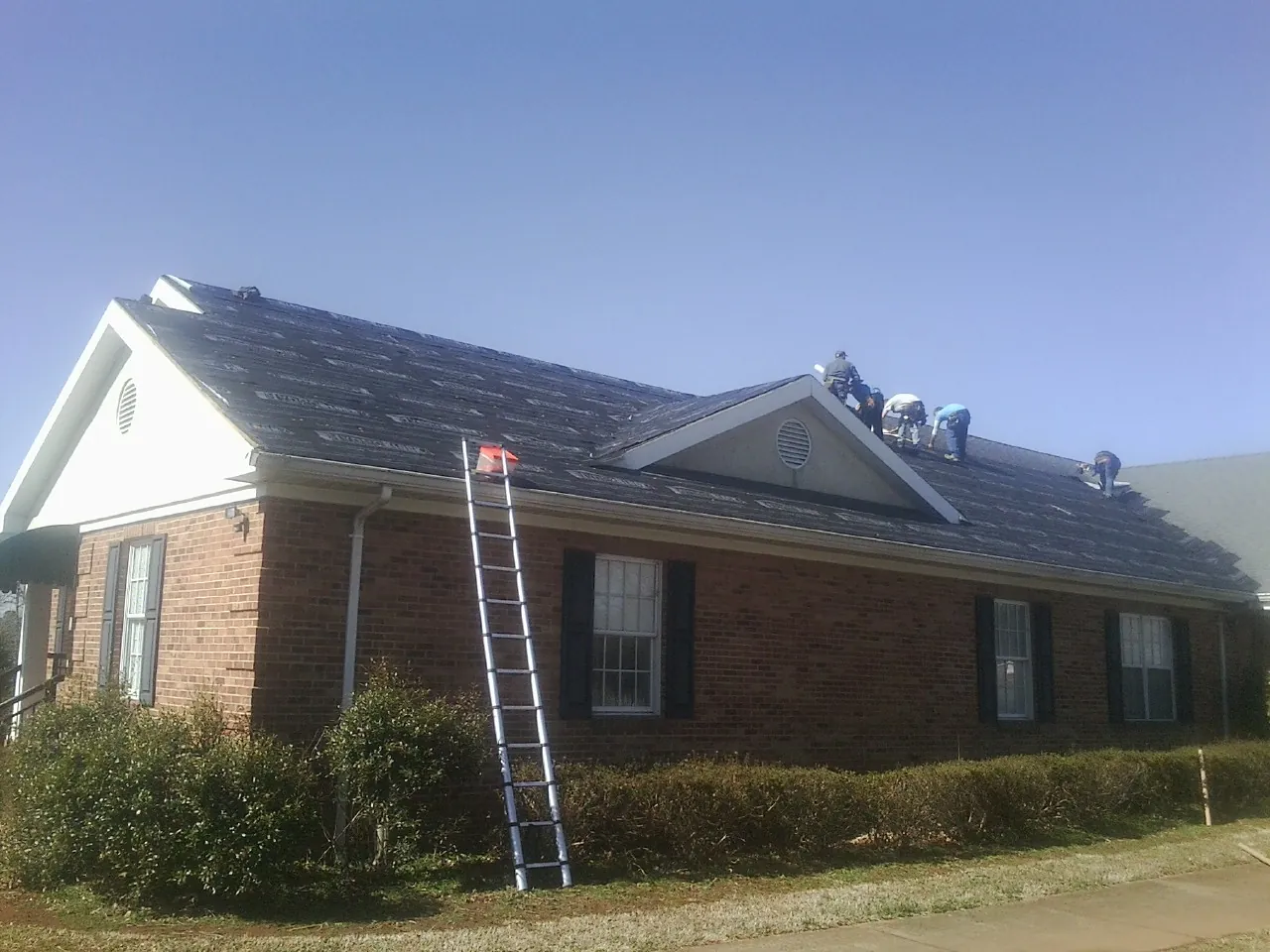Crew tearing shingles off a brick ranch roof with a ladder set — Metal Roof Repair work by our crew in Old Westbury