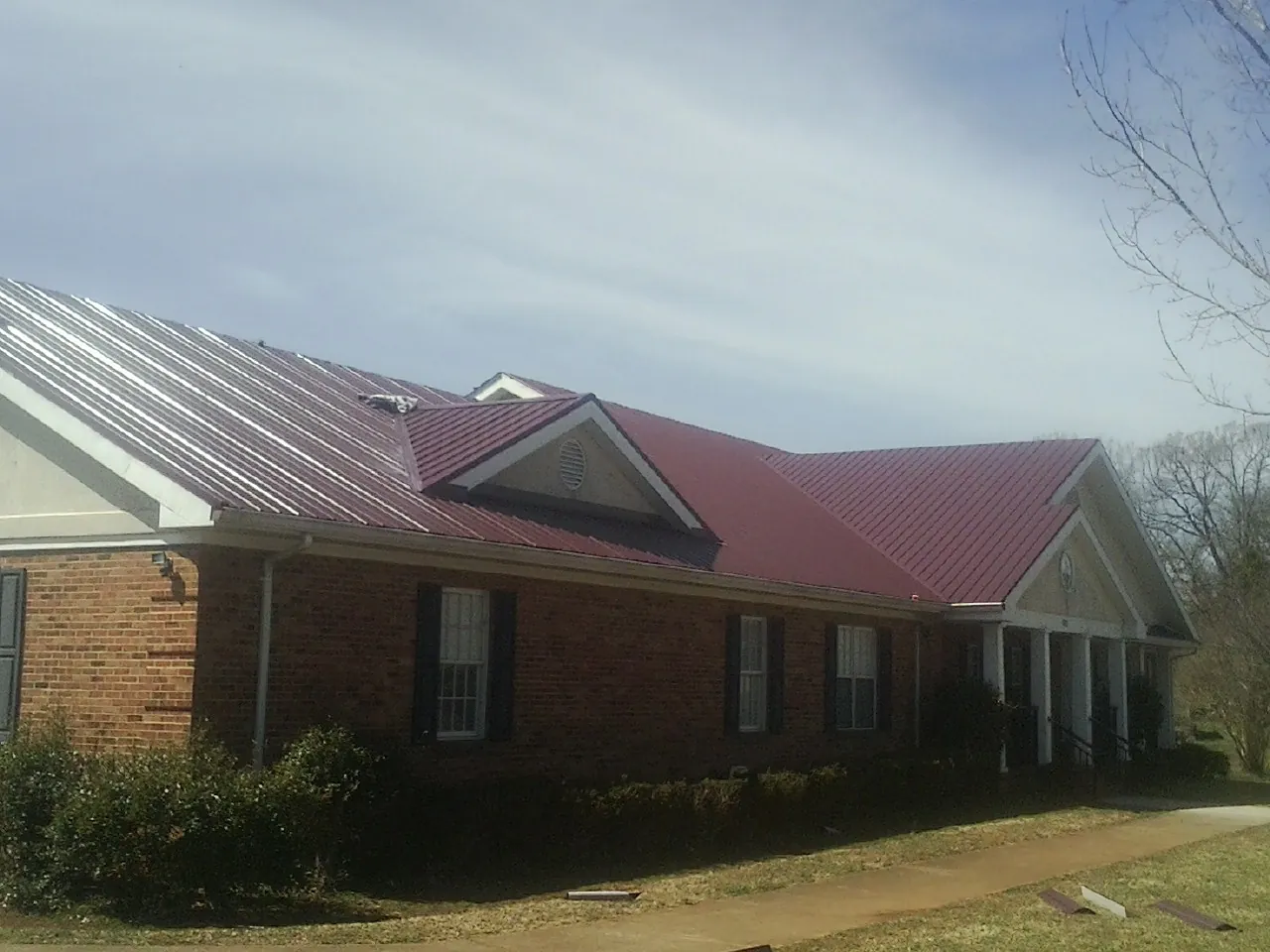 Red metal roof with gabled entries on a long brick building, from a Hail Damage Roof Repair job in Old Westbury