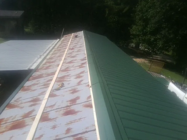 Old rusted panels beside newly installed green metal roofing — Wind Damage Roof Repair by Roofing Brothers in Old Westbury