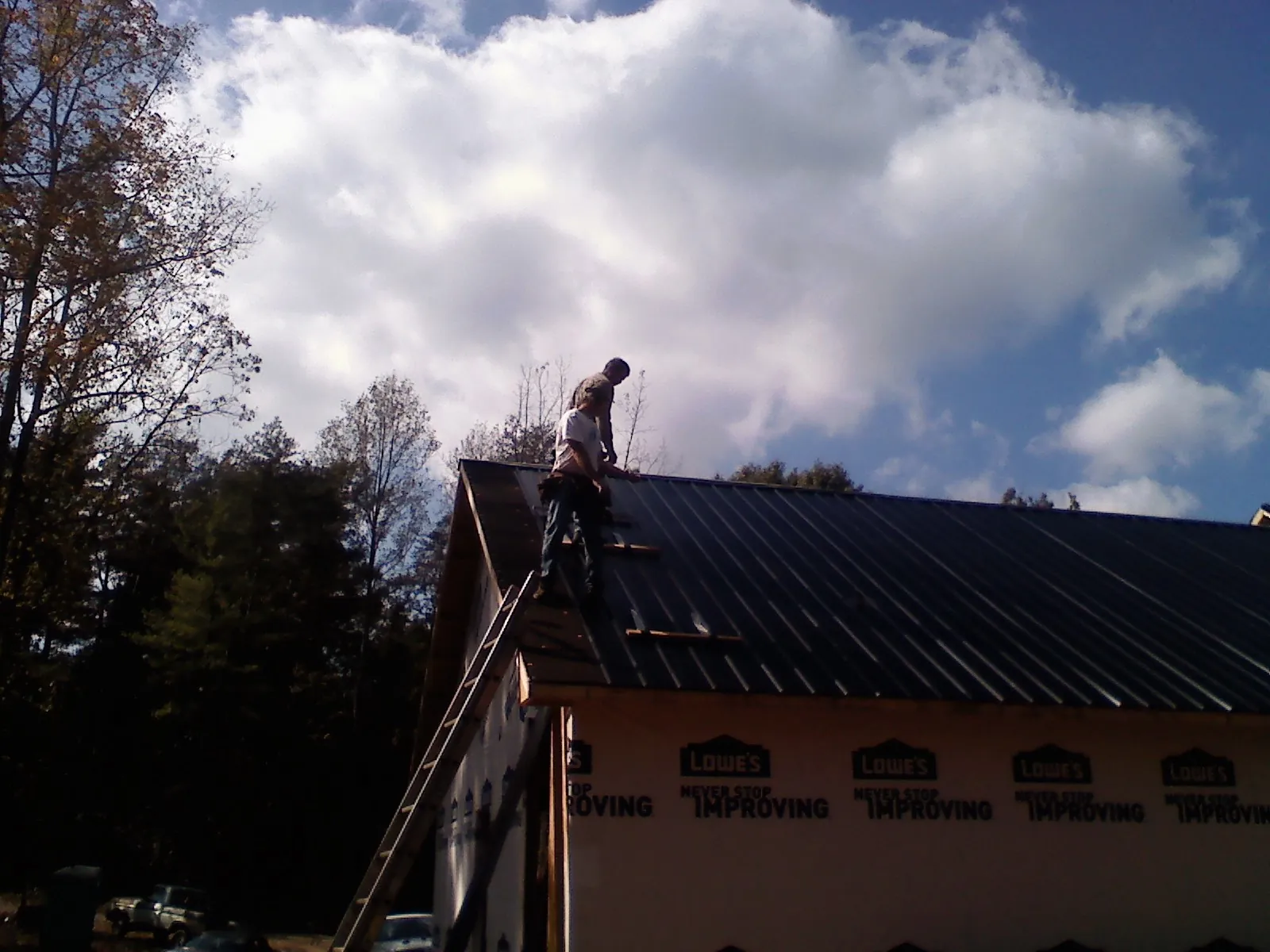 Roofer fastening dark metal panels high against a cloudy sky, from a Roof Inspection job in Old Westbury