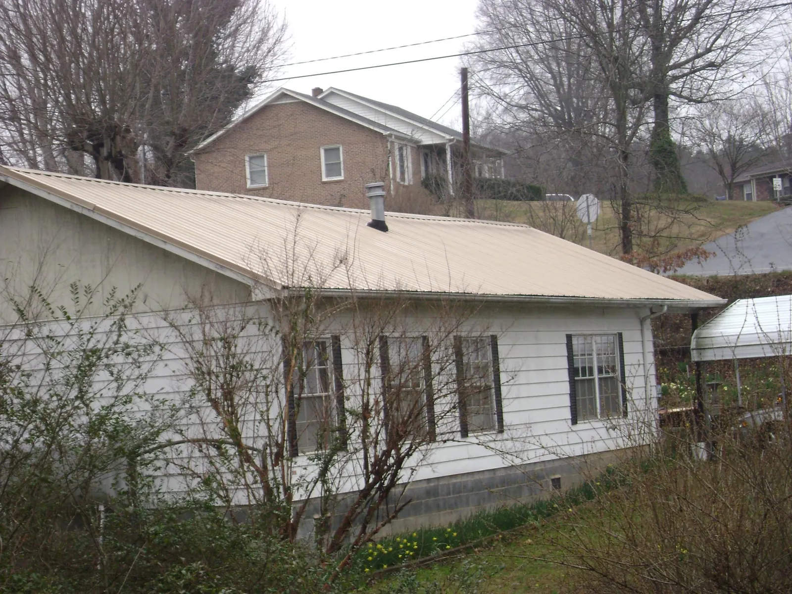 Tan metal roof on a white sided house set into a hillside — Commercial Roofing by Roofing Brothers in Old Westbury
