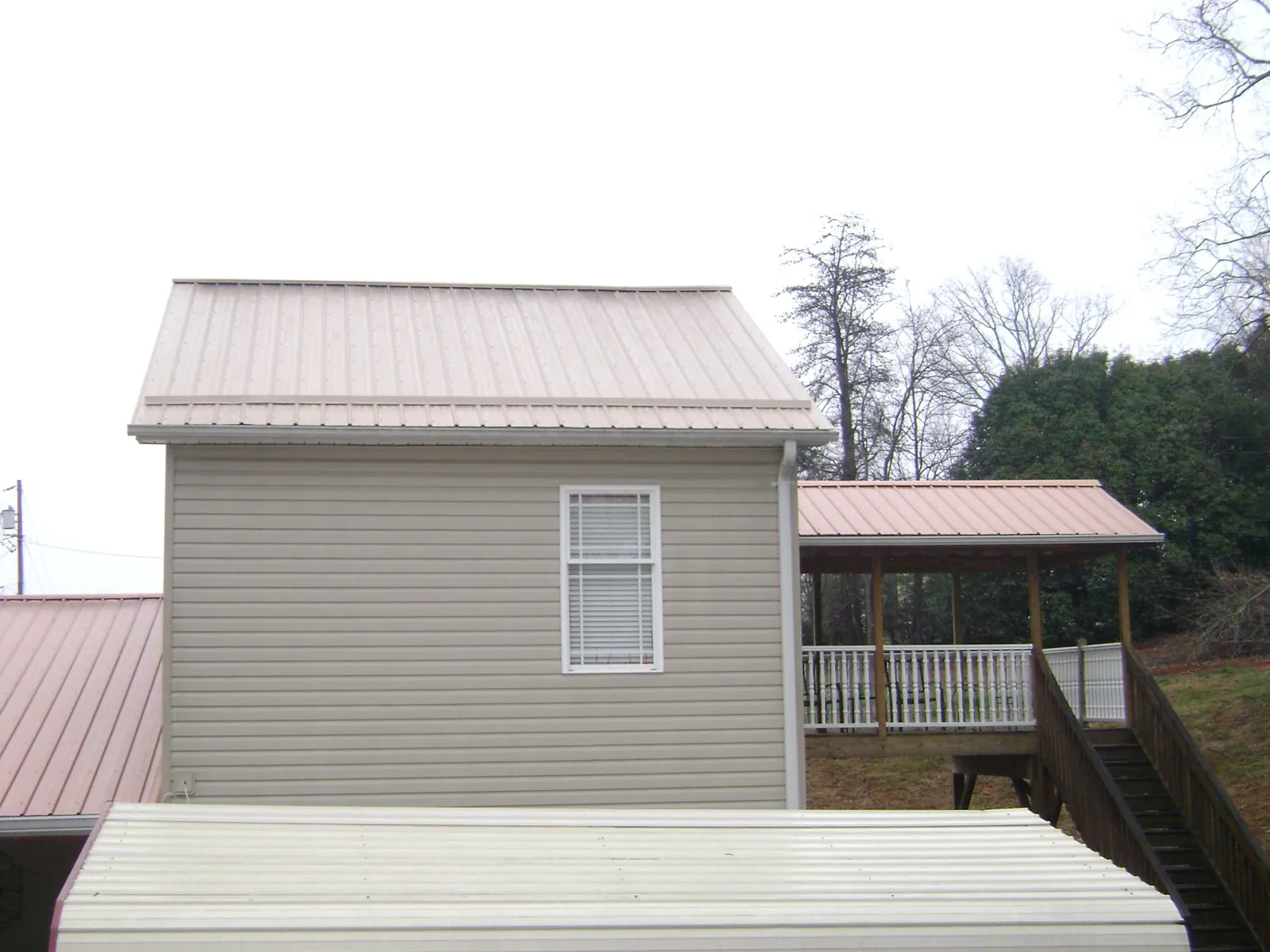 Tan metal roofs on a two story addition and attached porch, from a Roof Replacement job in Old Westbury