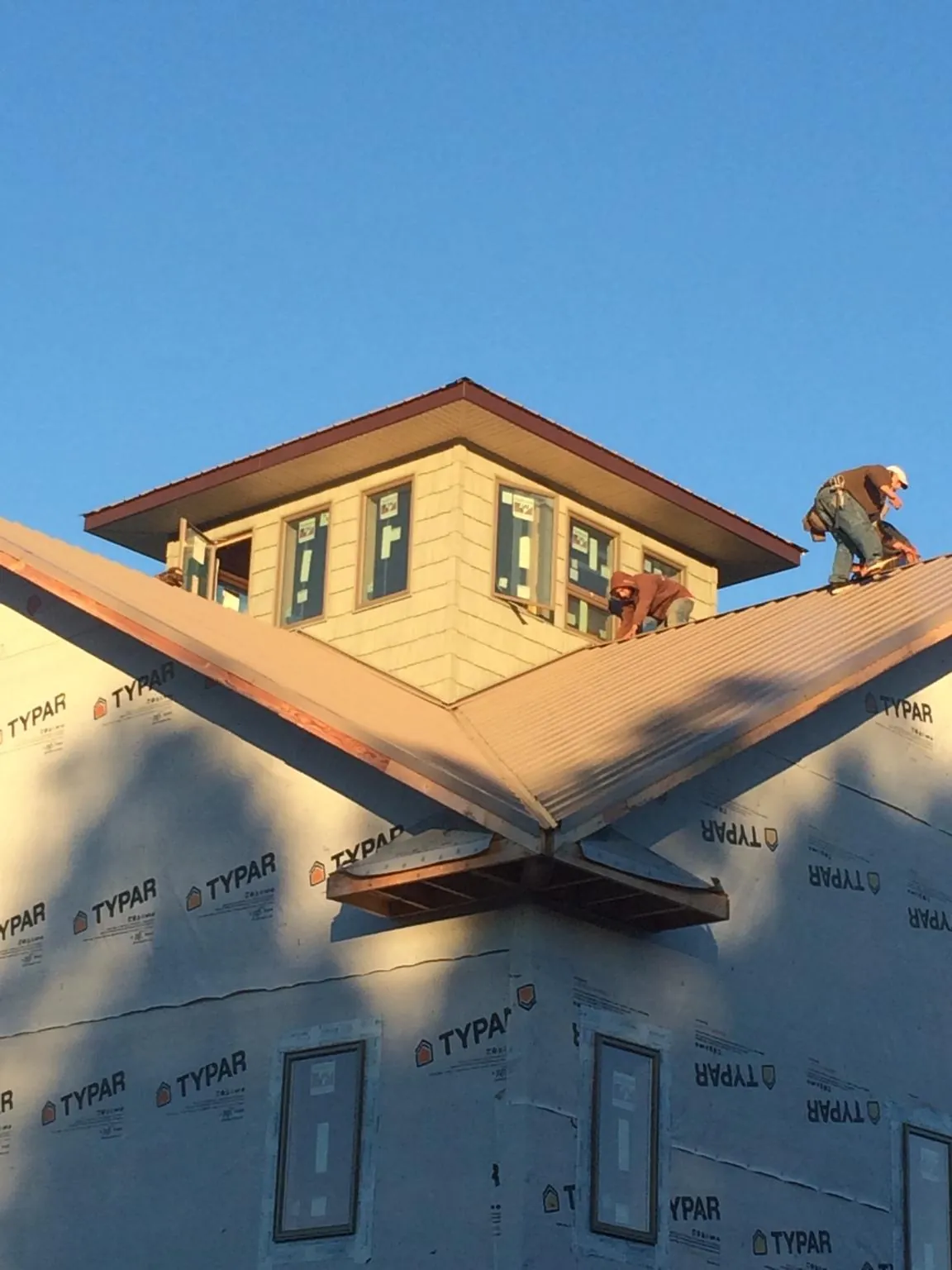 Roofers working around a rooftop cupola on a new metal roof at sunset — Roof Waterproofing in Old Westbury by Roofing Brothers
